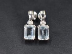 A pair of 18ct white gold stud earrings having small collared diamond drops to baguette cut Aqua
