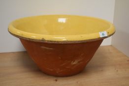 A large antique terracotta bowl with yellow glaze to inside.