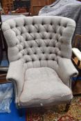 A traditional wing back armchair having button back tweed upholstery