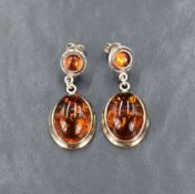 A pair of amber and silver drop earrings, having circular bezel set amber cabochons attached to