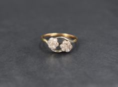 A floral diamond ring having two seven diamond set flower motifs with crossover shoulders on a