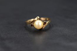 A cultured pearl ring having central pearl flanked by two small garnets to crossover shoulders on