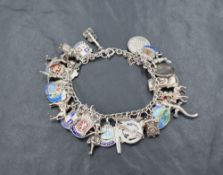 A white metal charm/shield bracelet having 34 charms, coins and enamelled shields, several stamped
