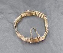 A yellow metal four bar gate bracelet marked 9ct, having a loop attachment and safety chain,
