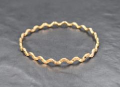 An Egyptian gold slave bangle of artisan form having cut and wave detail, bearing marks possibly