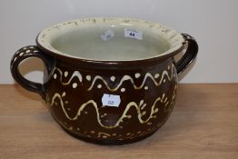 A Victorian slipware chamber pot with two strap handles and slogan to the rim, the interior with