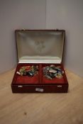 A red faux leather jewellery box containing a collection of costume jewellery including brooches