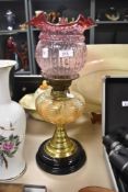 A vintage oil lamp having ceramic black base, amber glass reservoir and cranberry glass shade.