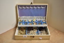 A large beige jewellery box containing an assortment of costume jewellery including brooches of