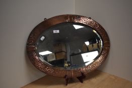An oval Arts and Crafts mirror in planished copper having four flat collars 57cm x 41cm approx.