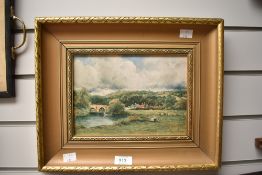 A framed coloured print of figures beside a river with stone arched bridge in the distance.