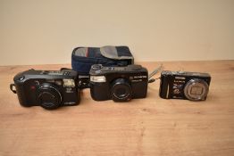 A Minolta Riva Zoom135EX AF camera, an Olympus Superzoom 70 camera, and a Lumix Power OIS camera