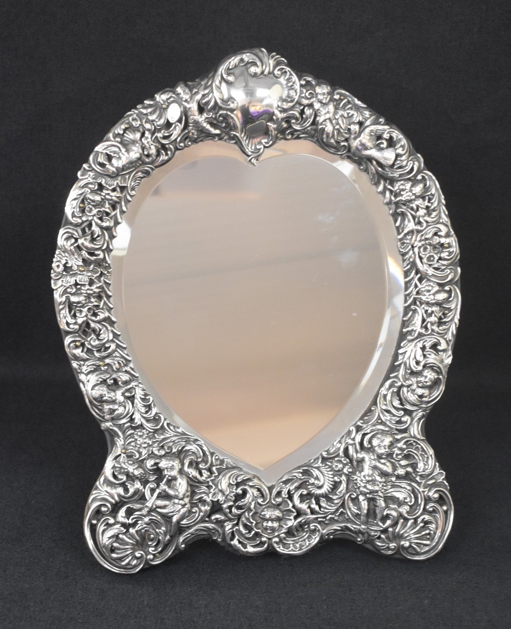 A late Victorian silver mounted heart shaped mirror, the embossed frame incorporating scroll work,