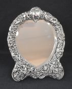 A late Victorian silver mounted heart shaped mirror, the embossed frame incorporating scroll work,