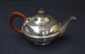 A George V silver teapot, of circular form having a curved generous spout opposed by a scroll