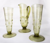 A Continental olive green glass jug and two flutes each with applied trailed decoration and prunts
