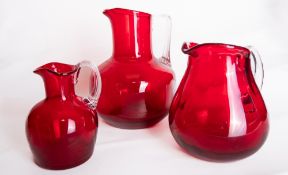 A group of three Whitefriars glass ruby red jugs, comprising a Cream jug with fluted body and