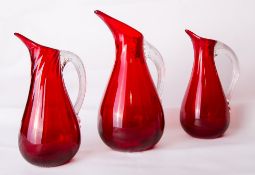A group of three Whitefriars glass ruby red 'Sparrow Beak' jugs, one large and two smaller, each