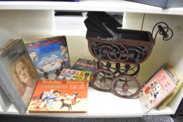 A miniature wicker dolls pram plant stand and a small selection of vintage children's books