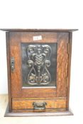 An Arts and Crafts oak smokers cabinet with embossed metal decoration to door, with internal