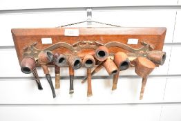 Ten vintage tobacco pipes, arranged in a wall hanging pipe rack.