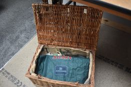 A picnik style wicker basket containing 2 cast pouches and a carrier bag with house of hardy printed