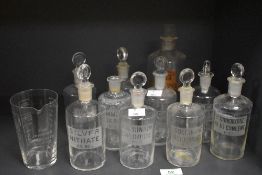 A group of ten clear glass chemist/apothecary bottles, nine with acid etched labels one with remains