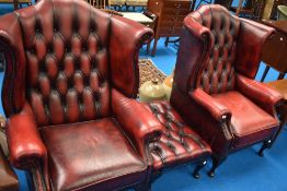 Two modern oxblood/red leather button wing back arm chairs and a similar footstool