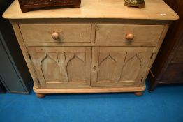 A stripped pine side cabinet having two drawers over double cupboard with gothic style panel to
