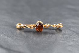 A yellow metal and citrine bar brooch, the central oval cut citrine in a claw setting, flanked by