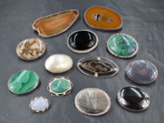 A selection of polished stone and shell set brooches, all in white metal mounts, most stamped silver