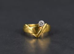 A yellow metal band ring stamped 18ct of stylised form having an inset collared diamond solitaire,