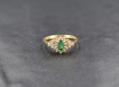 An emerald and diamond cluster ring, the central oval cut emerald measuring approximately 0.40ct