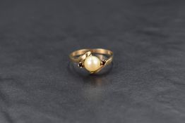 A cultured pearl ring having central pearl flanked by two small garnets to crossover shoulders on