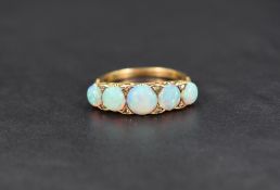 A five stone graduated opal ring having diamond chip points in a scroll pierced gallery mount on