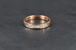 A 9ct rose gold band, set with seven round cut diamonds in a tension setting, ring size O-P, 2.9g