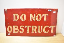 An enamelled rectangular sign, gold on red, 'Do Not Obstruct' and measuring 32cm x 65cm overall