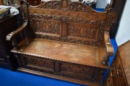 An early 20th Century oak box settle, having carved decoration to panels, width approx. 132cm