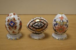 Three Royal Crown Derby porcelain eggs on stands, each with gold coloured stoppers and measuring