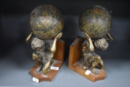 A pair of decorative cast gilt metal and mahogany figural bookends, formed as Atlas crouching with