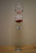 A modern clear glass and red sand egg timer, encased in a water filled clear glass cylinder, when