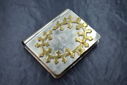 A white metal cigarette case of hinged rectangular book form, having applied brass decoration