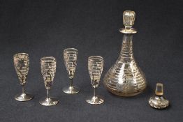 A glass liqueur decanter having white metal overlay depicting flowers, with four glasses having