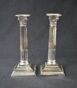 A pair of silver plated Corinthian column candlesticks, having concave square detachable sconces