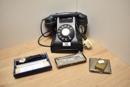 A black bakelite rotary telephone, sold together with a 1930s/40s white metal cigarette case, a