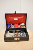A black faux leather jewellery box, having red lining, containing an assortment of costume jewellery
