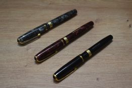Three Burnham B48 lever fill fountain pens in red marble, grey marble and black with one broad