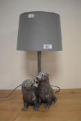 A contemporary table lamp incorporating a pair of otters in silvered finish.