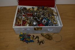 A cream jewellery box having gold decoration and red lining, containing an assortment of costume