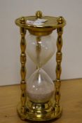 A brass and glass egg timer, of traditional hour glass form with brass surmount and base with